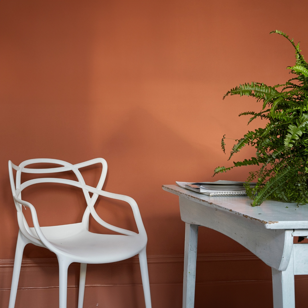 A modern white chair and shabby-chic desk in front of a bright, warm orange